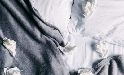 There are a few used tissues lying on a rumpled bed.