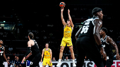 Photo: Game scene in a dark hall. Players in black and yellow jerseys, one person jumping for the ball.